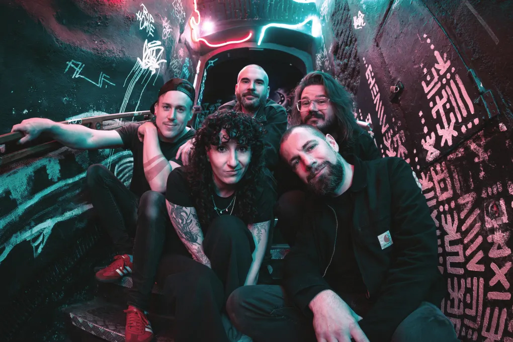Promotional photo of the band Melonball sitting on a neon-lit stairway