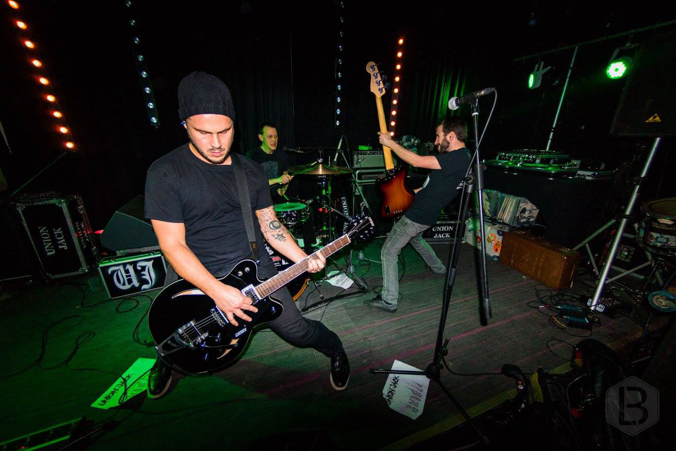 Union Jack performing live on stage, with guitarist, drummer and bassist playing under green and red concert lights.